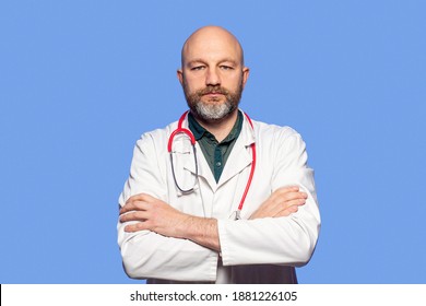 Portrait of bald slim doctor wearing white uniform, green shirt, red stethoscope and glasses on blue background. Caucasian in 40s, grey beard, hands crossed - Powered by Shutterstock