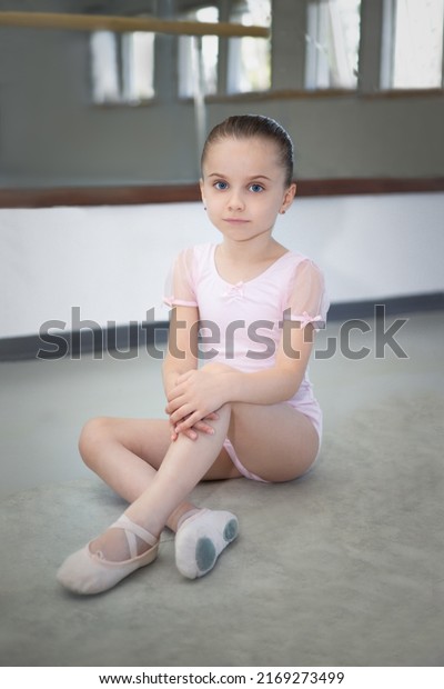Portrait of a ballerina girl\
sitting and resting on the floor and looking into the lens. Ballet\
pump
