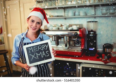 Portrait of barista holding Christmas sign at cafe against snow falling - Powered by Shutterstock