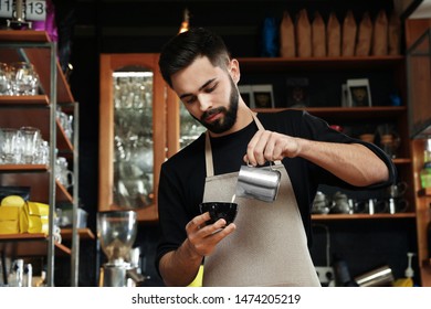 Portrait Of Barista Pouring Milk Into Cup Of Coffee Against Bar Shelves In Cafe