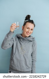 Portrait Of A Beaming Woman Raising A Glass Of Water. Golden Glitter On Her Cheeks. Over Blue Background.