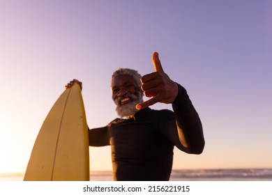 Portrait Of Bearded African American Senior Man With Surfboard Gesturing At Beach Against Clear Sky. Copy Space, Happy, Unaltered, Retirement, Aquatic Sport, Holiday And Active Lifestyle Concept.