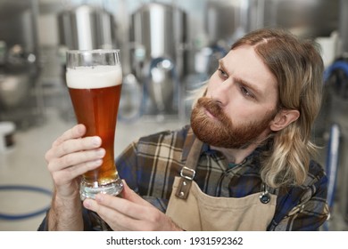 Portrait of bearded brewmaster holding beer glass while inspecting quality of production at brewing factory, copy space - Powered by Shutterstock