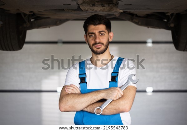 Portrait of bearded handsome automotive mechanic\
man standing in garage. Vehicle service manager worker work in\
mechanics workshop looking at camera after check and maintenance to\
repair the engine.