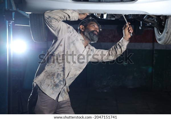 Portrait\
of bearded happy car mechanic in a car service station examining a\
lifted car. Car Specialist Professional repairman is smiling and\
working dedicatedly in a modern clean\
workshop.