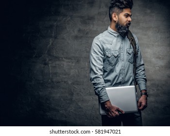 Portrait of bearded Indian male holds a laptop.