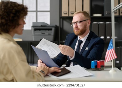 Portrait of bearded male consultant working in US embassy office and holding application form while talking to woman - Shutterstock ID 2234701527