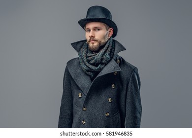 Portrait of bearded male dressed in a grey jacket and a hat isolated on grey background.