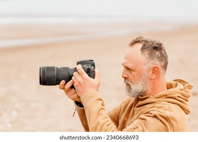 portrait of a bearded man photographing the sea on the beach in autumn - Powered by Shutterstock