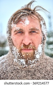 Portrait Of Bearded Man With Snow On His Face. Man Is Frozen In Pullover With Hood.