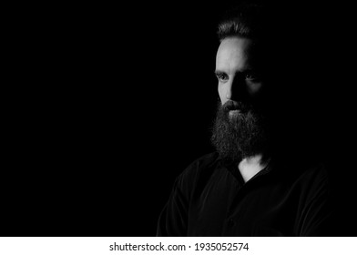 Portrait Of A Bearded Man In A Studio Environment In Front Of A Black Background With Dramatic Low Key Lights.