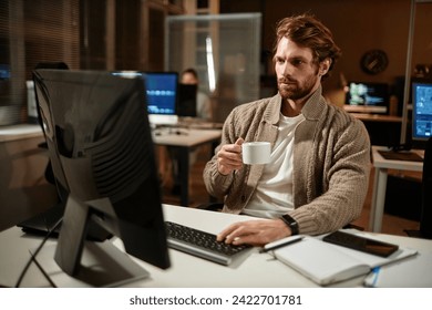 Portrait of bearded man using computer in office and drinking coffee while working late at night, copy space - Powered by Shutterstock