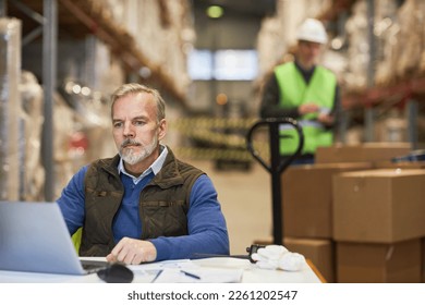 Portrait of bearded mature man using laptop in storage warehouse while managing shipping and distribution business - Powered by Shutterstock