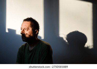 Portrait of bearded middle-aged man with dramatic and intense gaze, deep shadows shaping his face against dark blurred interior. Selective focus.