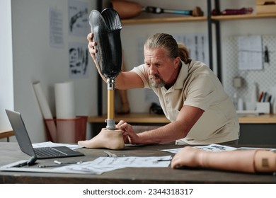 Portrait of bearded senior man inspecting leg prosthetics in workshop doing measurements and quality control - Powered by Shutterstock