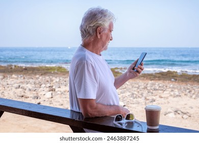 Portrait of bearded senior retired man outdoors at the seaside beach talking on mobile phone enjoying free time and relaxed vacation. Horizon over water - Powered by Shutterstock