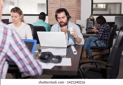 Portrait Of Bearded Spanish Man In Headphones Working On Laptop In Busy Modern Coworking Office