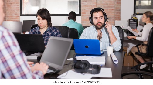 Portrait Of Bearded Spanish Man In Headphones Working On Laptop In Busy Modern Coworking Office