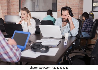 Portrait Of Bearded Spanish Man In Headphones Working On Laptop In Busy Modern Coworking Office