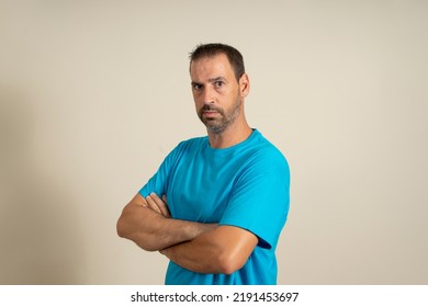 Portrait Of A Bearded Spanish Man Posing With His Arms Crossed While Looking At The Camera Very Serious, Isolated Over Beige Background.