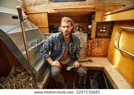 Portrait of bearded young man repairing boat engine and looking at camera in sunlight, copy space