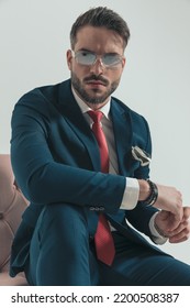 Portrait Of Bearded Young Man In Suit Holding Elbow On Knee And Posing In A Fashion Way In A Cut Out Picture In Studio