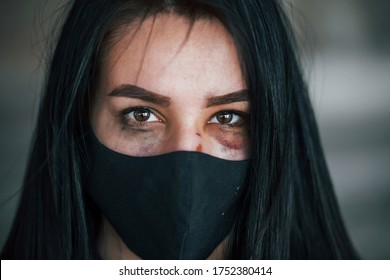 Portrait Of Beaten Young Woman In Black Protective Mask With Bruise Under Eye Indoors In Abandoned Building.