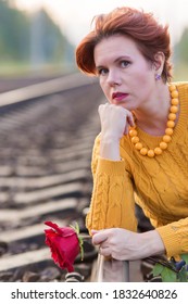 Portrait Of Beautiful 30 Year Old Woman Sitting On Rails Of The Railway Holding Red Rose