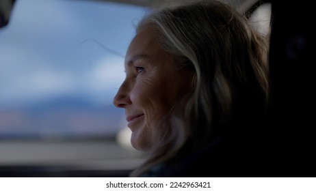 Portrait of beautiful 60s mature senior grey haired Caucasian female riding in a car on a passenger seat with opened window - Powered by Shutterstock