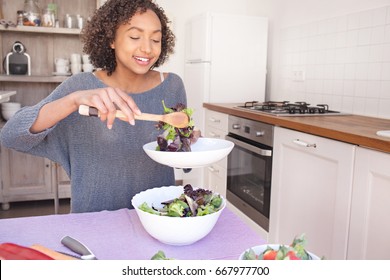 Portrait Of Beautiful African American Adolescent Girl Serving Salad, Eating Fruit And Vegetables In Home Kitchen, Smiling Indoors. Young Black Woman Cooking Healthy Vegan Food, Lifestyle In Interior.