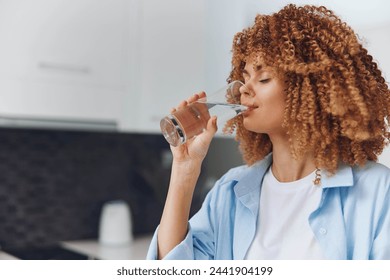 Portrait of beautiful African American woman drinking water from a glass in the kitchen at home - Powered by Shutterstock