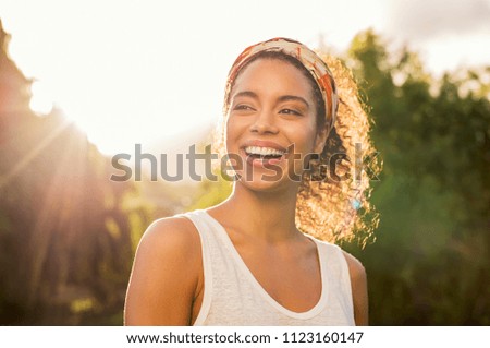 Photo of Portrait of beautiful african american woman smiling and looking away at park during sunset. Outdoor portrait of a smiling black girl. Happy cheerful girl laughing at park with colored hair band.