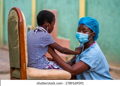 Portrait Of A Beautiful African Health Care Provider Wearing Scrubs And Face Mask For Protection And Looking At Camera With A Child Patient Hands Placed On Her Shirt-concept On Black Millennial Health