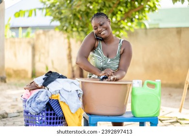 portrait of beautiful african lady washing and communicating on smartphone- manual cloth washing outdoor - Powered by Shutterstock