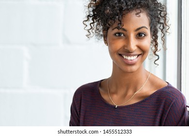 Portrait of a beautiful african woman smiling. Young black woman in casual looking at camera with copy space. Portrait of cheerful girl with afro hair sitting near a window.