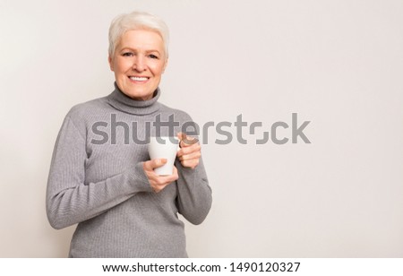 Portrait of beautiful aged woman holding cup with hot drink trying to warm up, free space