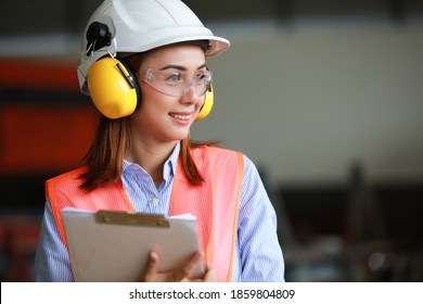 Portrait Beautiful Asia Engineer Wearing PPE Safety Helmet , Safety Glasses , 
Safety Vest And Earmuff Work In Factory