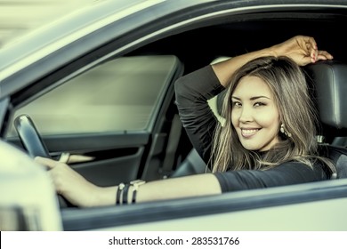 Portrait Of Beautiful Asian Brunette Young Woman Keep Wheal Inside New Luxury Car Through Transparent Window Background Copy Space For Inscription Taxi Girl Empty Place Female Rest Indoor Smiley Face 