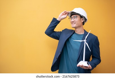 Portrait Beautiful Asian Engineer Man Architect Standing Yellow Background Holding Small Wind Turbine,Solar Panel, Cell.Renewable Energy Sustainability Concept.Banner Cover Design For Electricity.