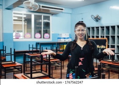 Portrait Of Beautiful Asian Female Teacher Wearing Face Shield Smiling While Standing  In Classroom. New Normal Lifestyle During Corona Virus Or Covid-19 Crisis