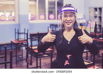 Portrait Of Beautiful Asian Female Teacher Wearing Face Shield Smiling And Thumbs Up Gesture With Hand While Standing In The Classroom. New Normal Lifestyle During Corona Virus Or Covid-19 Crisis