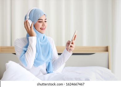 Portrait of beautiful asian muslim female in sleepwear watching online story on mobile phone, lites on bed and connected with wireless internet. Young cute girl with hijab listen music from smartphone - Powered by Shutterstock