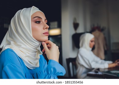 Porträt eines schönen asiatischen Moslemmodells mit weißer Bluse und blauem Hijab, das auf weißem Vorhang als Hintergrund in Nahaufnahme steht.