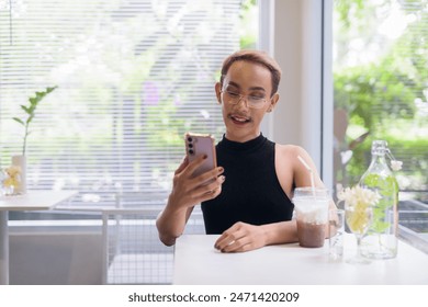 Portrait of beautiful Asian queer LGBT community supporter man with mustache wearing lipstick and jumpsuit using mobile phone in coffee shop - Powered by Shutterstock