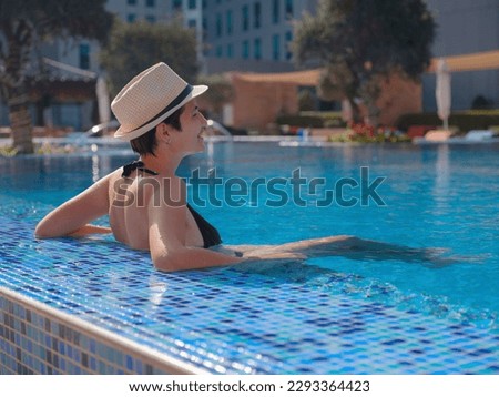 Portrait of beautiful asian woman in black swimwear and hat relaxing in swimming pool spa. Hot summer day and bright sunny light. Healthy body care in travel
