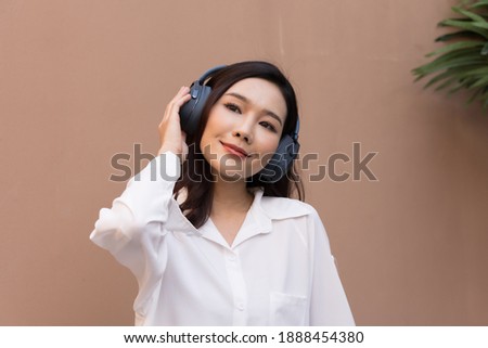 Portrait of a beautiful Asian woman with healthy skin. She was wearing a white sweater. She listened to music on the headphones and danced with joy. isolated on brown background