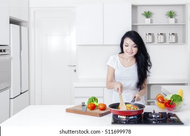 Portrait Of A Beautiful Asian Woman With Long Hair, Cooking Vegetable With A Frying Pan On The Stove