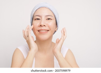 Portrait Of A Beautiful Asian Woman With No Makeup Tapping Finger On Her Cheek To Apply Daily Facial Skincare And Feeling Happy For Her Smooth, Soft And Clean Face. K Beauty, Glowing, Anti-aging, 40s.