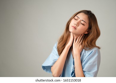 Portrait of a beautiful Asian woman in patient gown raised her hands and touch her neck feeling like pain from office syndrome on gray background with copy space, concept healthcare insurance.