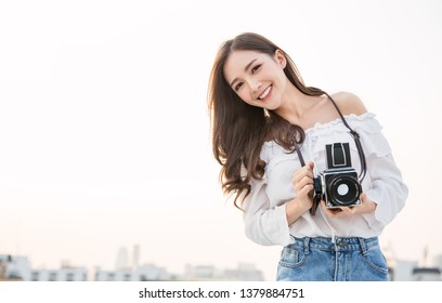 Portrait of beautiful asian woman photographer fashion look taking photo. Pretty cool young woman model with retro film camera curly hair, solo traveler outdoors over rooftop sky with copy space - Powered by Shutterstock